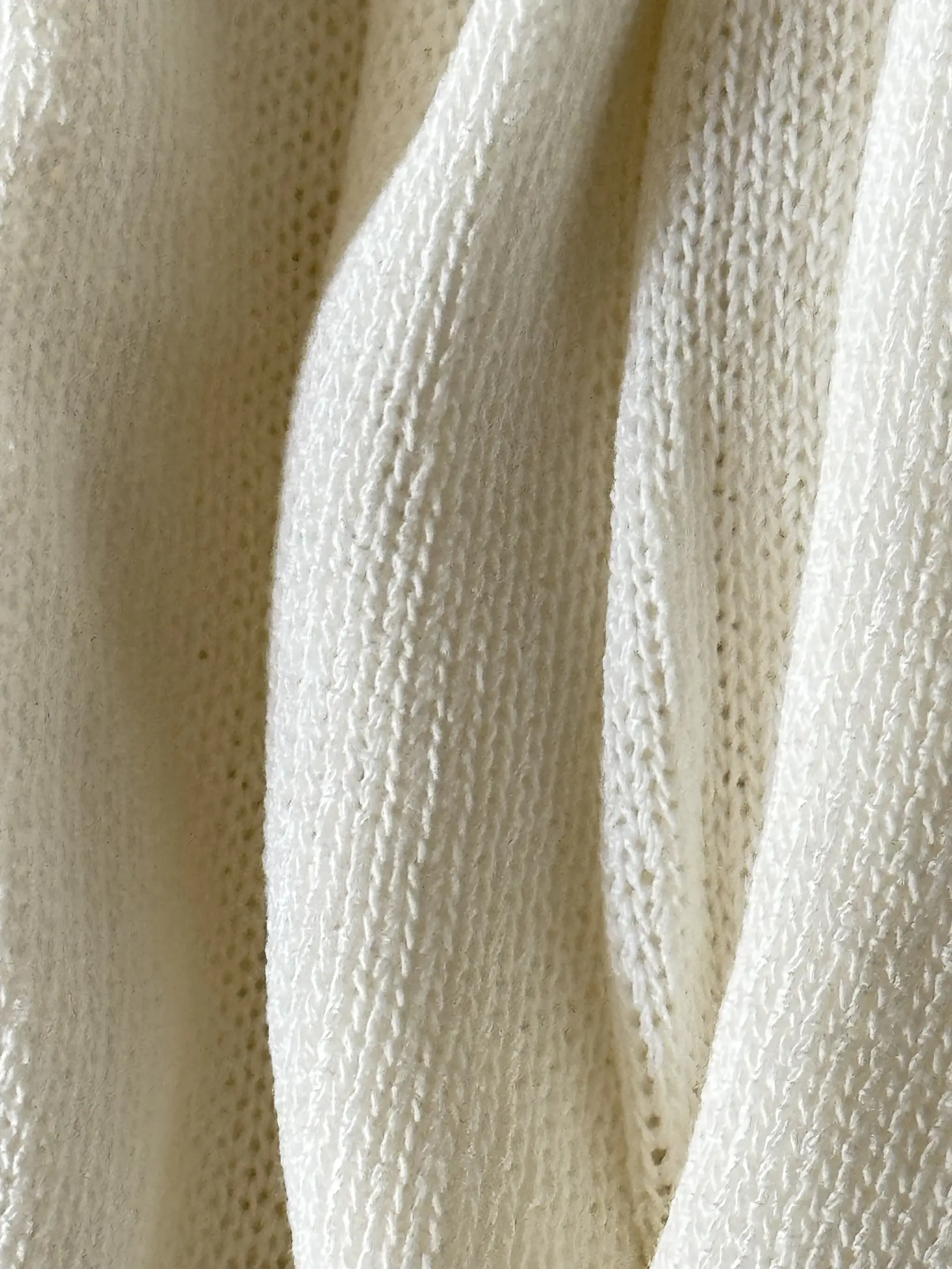 Fine cream knitted textile hanging vertically